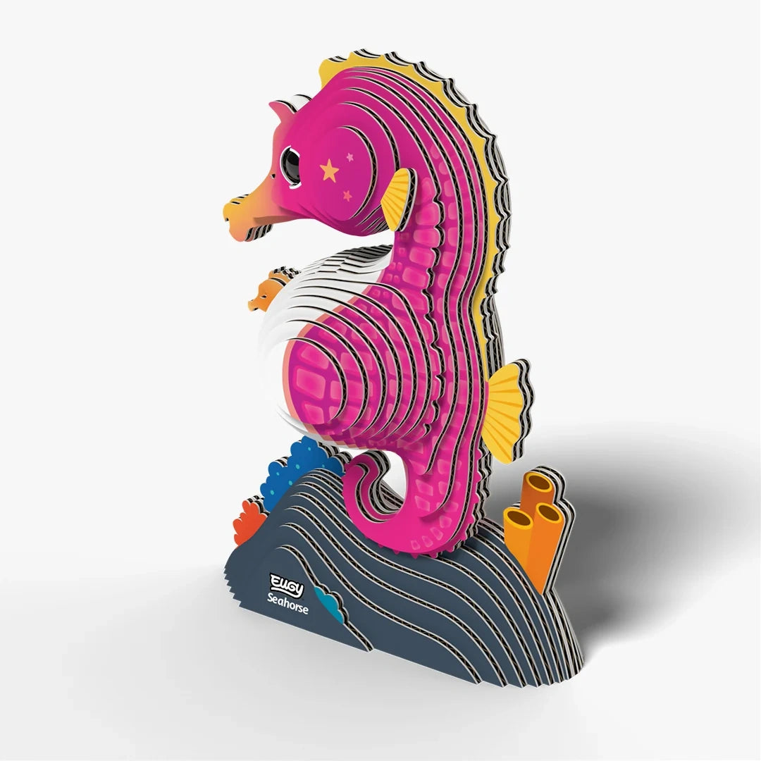 EUGY Seahorse pink cardboard model viewed at an angle showing its curved back, yellow dorsal fin, curled tail and orange coral tubes