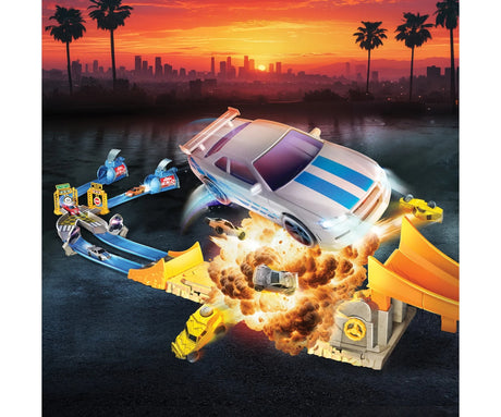 Fast & Furious Nitro Blast promotional scene with a large silver car jumping above an explosion, smaller cars flying through the crash zone, blue racing tracks and an orange ramp against a sunset city skyline.