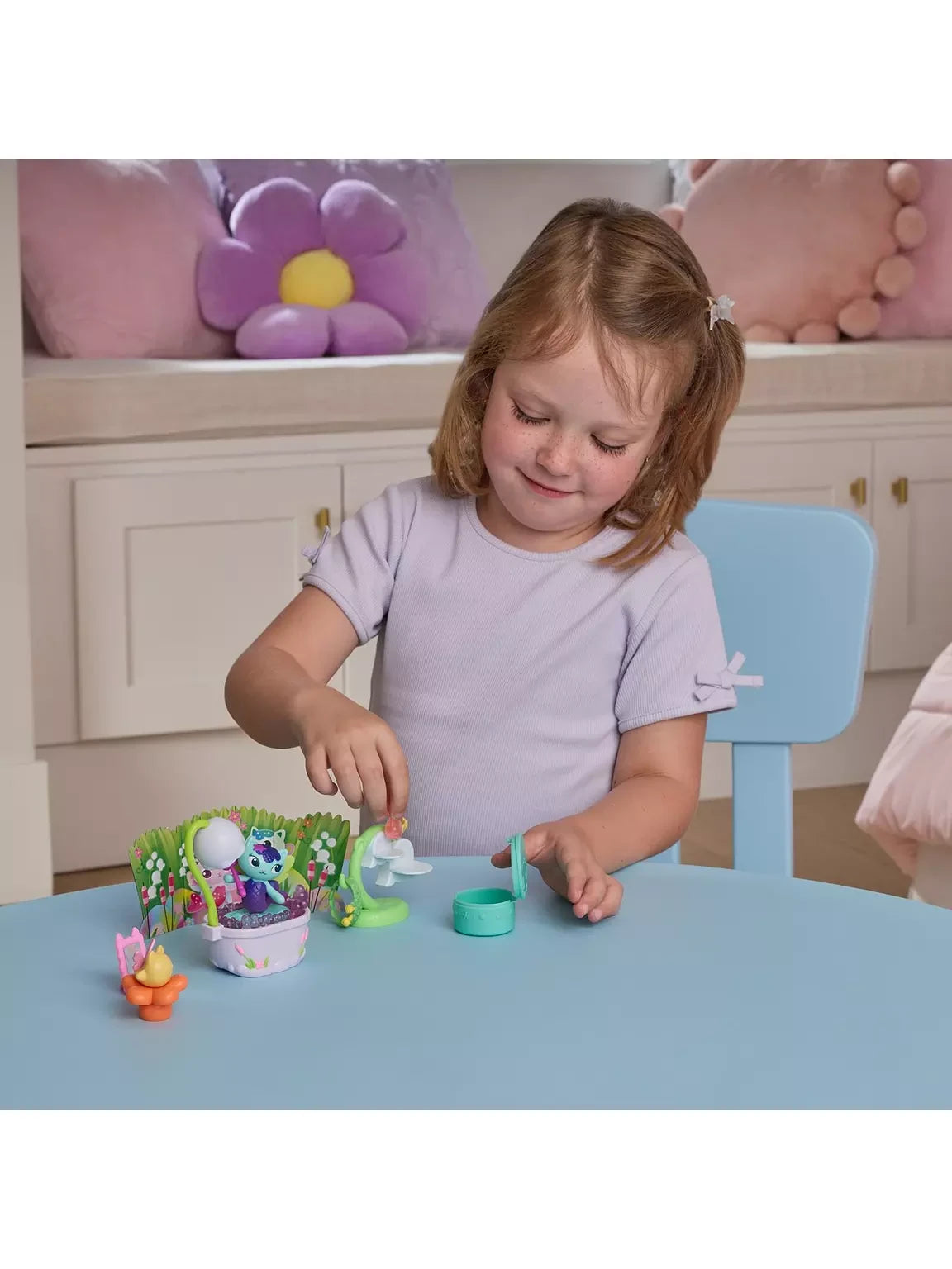 Child playing with the MerCat bathtub, green bathroom stand, pink mirror, orange flower seat and turquoise container on a blue table