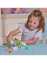 Child holding the white shower head over MerCat in the lavender bathtub with the green bathroom stand and accessories arranged beside it