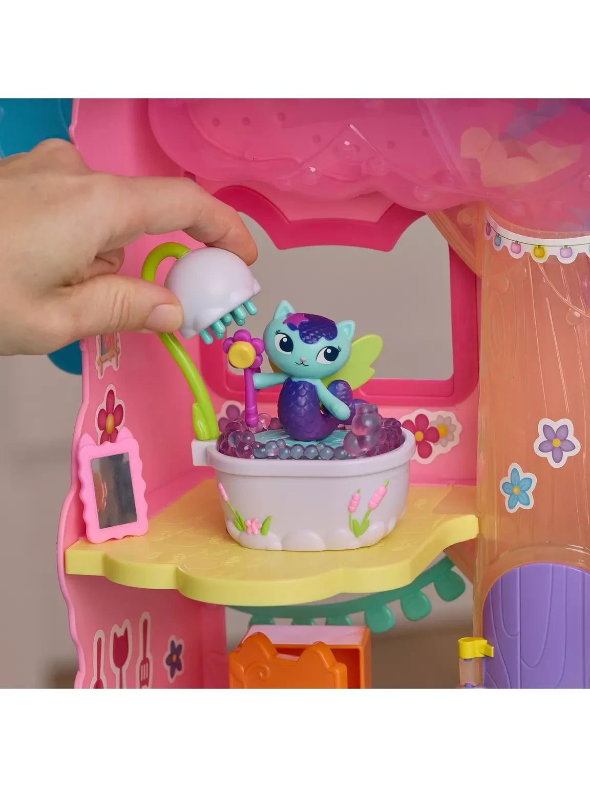 Hand holding the white shower head over MerCat in the lavender bubble bathtub inside a pink Gabby's Dollhouse room