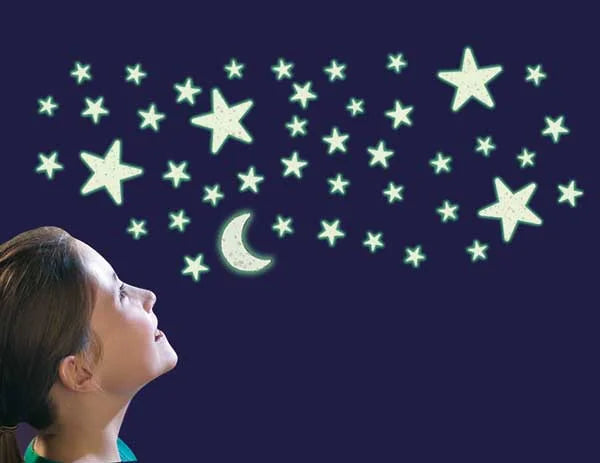 Bedroom scene with child looking up at glowing glitter stars and moon stickers shining on a dark wall.