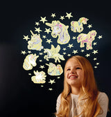 Smiling girl looking up at glowing unicorn and star stickers arranged on a dark wall in a circular pattern