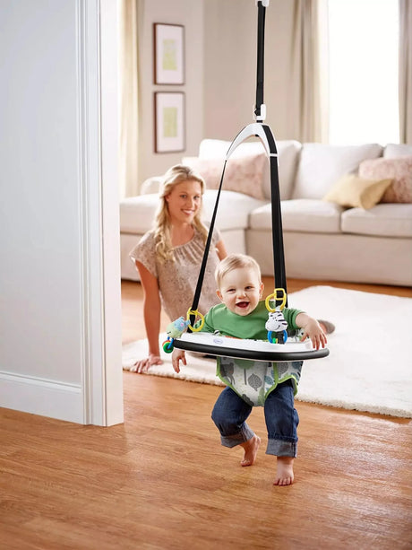 Baby bouncing and smiling in a Graco doorway jumper with toy attachments, hanging from door frame with parent watching in background