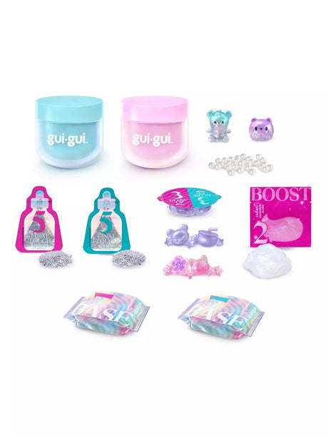 Gui Gui Deluxe Twin Pack complete contents laid flat showing teal and pink jars, two teal and purple mini figurines, pearl beads, two sparkle sachets with glitter, glow up charm tray with cat and bat figures, booster sachet, booster slime blob and two iridescent base sachets