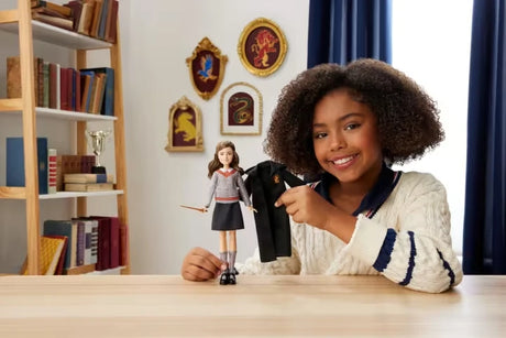 Child holding the removable Gryffindor robe beside the Hermione Granger fashion doll