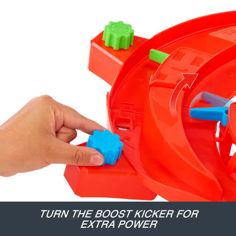 Close-up of a hand turning the blue boost kicker on the curved red Hot Wheels Formula 1 track, with a green adjustment knob and directional arrow showing the track mechanism.