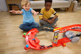 Two boys sitting on a wooden floor playing with the Hot Wheels Formula 1 Downhill Circuit Race set, featuring the red and black curved racing track, three miniature F1 cars and upright lap counter.
