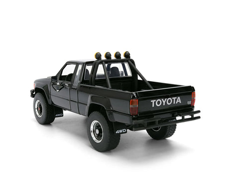 Jada Toys black 1985 Toyota SR5 Pickup shown from the front and side, featuring raised suspension, large tyres, front lights and a black grille.