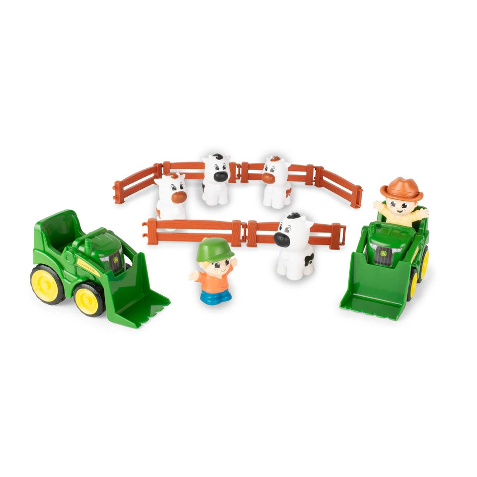 John Deere farm toy playset with two green front loader tractors, four white cow figures, orange fence corral pieces and two farm figures on white background