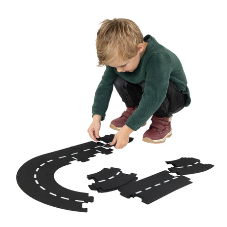 Child assembling the Kids Globe 18 Piece Car Track Road Division by connecting black road puzzle pieces on the floor