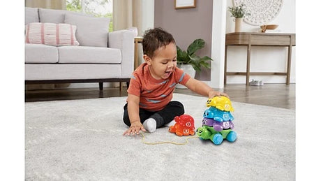 Child sitting on rug beside LeapFrog Nest & Count Turtle Tower with stacked turtles and pull string
