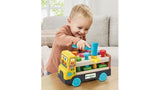 Young boy smiling while holding the blue hammer above the LeapFrog Pound & Pop Truck, with colourful pegs and the yellow truck cab visible.