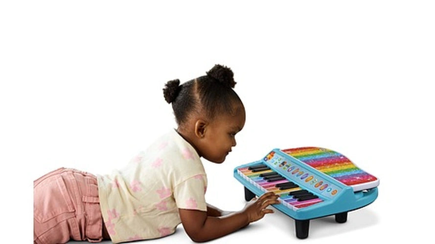 Young girl lying on her stomach and pressing the keys of a LeapFrog Twinkle Lights Learning Piano