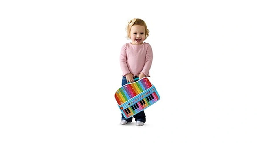 Smiling toddler wearing a pink jumper holding the LeapFrog Twinkle Lights Learning Piano by its carrying handle