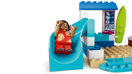 LEGO Lilo figure seated on a blue slide beside a beach sign and surfboard