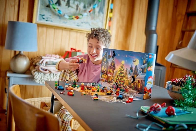 Child reaching toward LEGO City Advent Calendar builds arranged in front of the opened snowy calendar