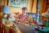 Child reaching toward LEGO City Advent Calendar builds arranged in front of the opened snowy calendar