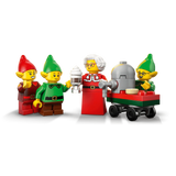 Mrs. Claus and three LEGO elves beside a red and green wheeled cart with a grey machine