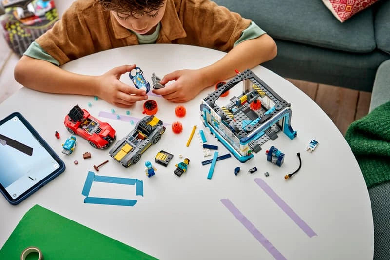 Child building a LEGO City car wash set at a table with cars, car wash model, pieces and tablet instructions