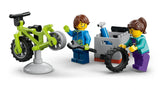 Two LEGO minifigures repairing a green mountain bike with a spare tyre and tool