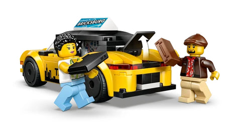 Rear angled view of the LEGO City yellow taxi with the rear trunk panel open upward, showing interior space, with two minifigures standing behind the vehicle holding rectangular luggage pieces