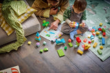 Child playing with LEGO DUPLO bricks and model builds beside an adult and an instruction booklet