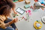 Person building a LEGO flower stem at a table with loose pieces and a finished flower display