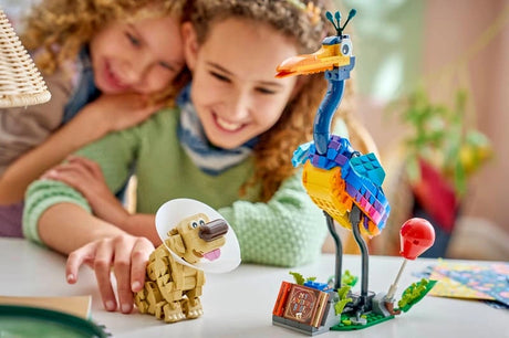 Two children smiling while examining the completed LEGO Disney Kevin and Dug models on a table, with Kevin's colourful feathers, red balloon and Dug's white cone visible.