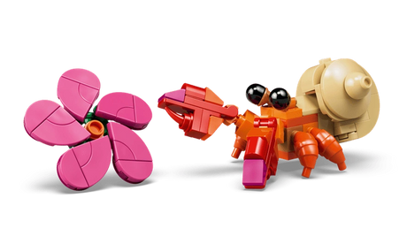 Close-up of the small orange LEGO Disney hermit crab with black eyes, beige shell and red claws beside a brick-built pink flower with five petals.