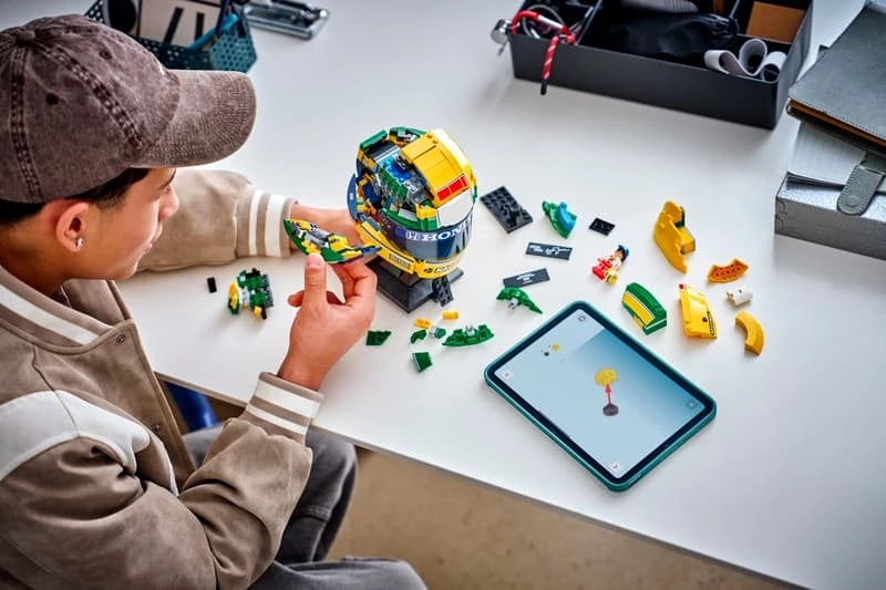 Person building LEGO Ayrton Senna Helmet 43024 at a desk with loose pieces and digital instructions on a tablet