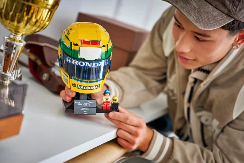 Person holding LEGO Ayrton Senna Helmet 43024 beside a trophy with Senna minifigure and plaque on the stand