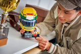 Person holding LEGO Ayrton Senna Helmet 43024 beside a trophy with Senna minifigure and plaque on the stand