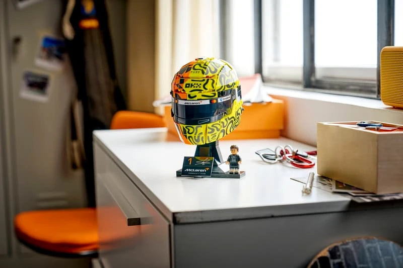 Completed LEGO Lando Norris Helmet displayed on a white desk beside the minifigure, signature plaque and loose stationery