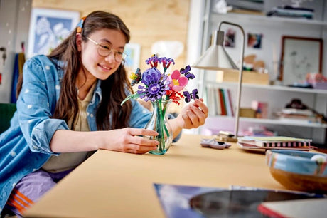 Young builder arranging the LEGO Editions Olivia Rodrigo's Flower Bouquet 11507 in a glass vase on a desk