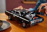 Person building LEGO Technic Dodge Charger R/T car at a table with model pieces visible