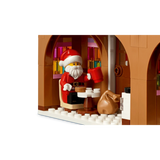 LEGO Santa minifigure seated inside the gingerbread house with a red mug, small table and brown sack