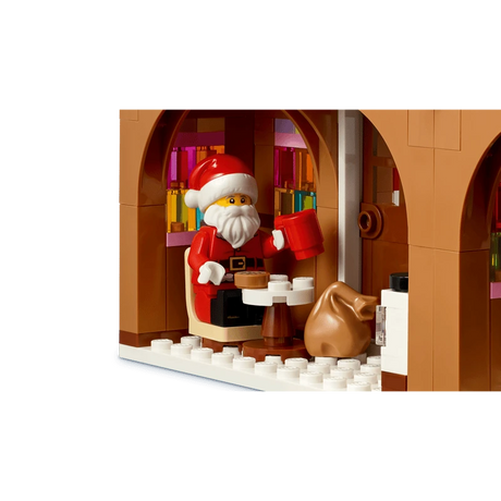 LEGO Santa minifigure seated inside the gingerbread house with a red mug, small table and brown sack