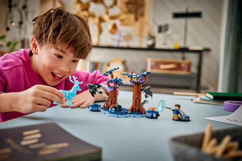 Child building a LEGO Harry Potter Forbidden Forest set at a table with tree pieces, minifigures and tablet instructions
