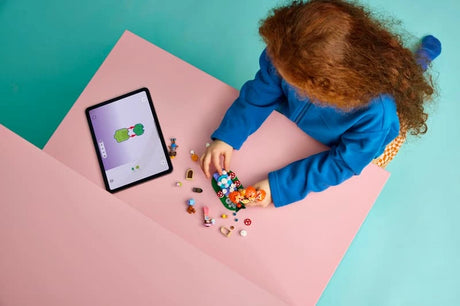 Child building LEGO Friends Forest Tea Party at a table with pieces and tablet visible