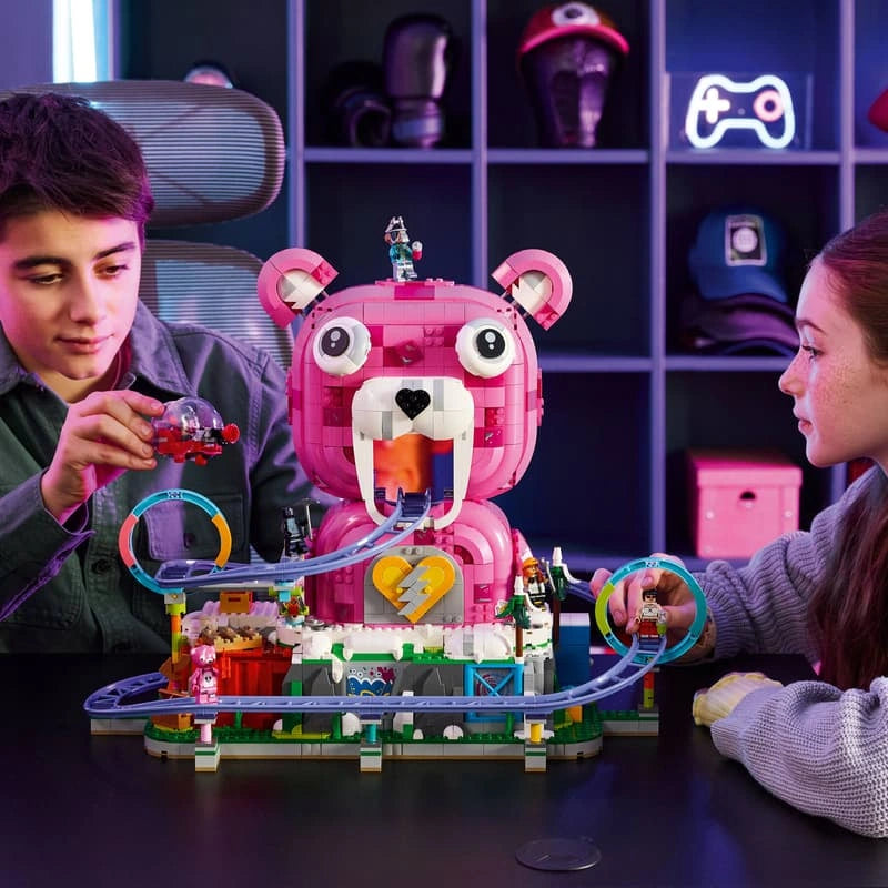 Two children playing with LEGO Fortnite Rave Cave 77082, featuring the pink Cuddle Team Leader bear head, purple roller coaster track and transparent coaster cart.