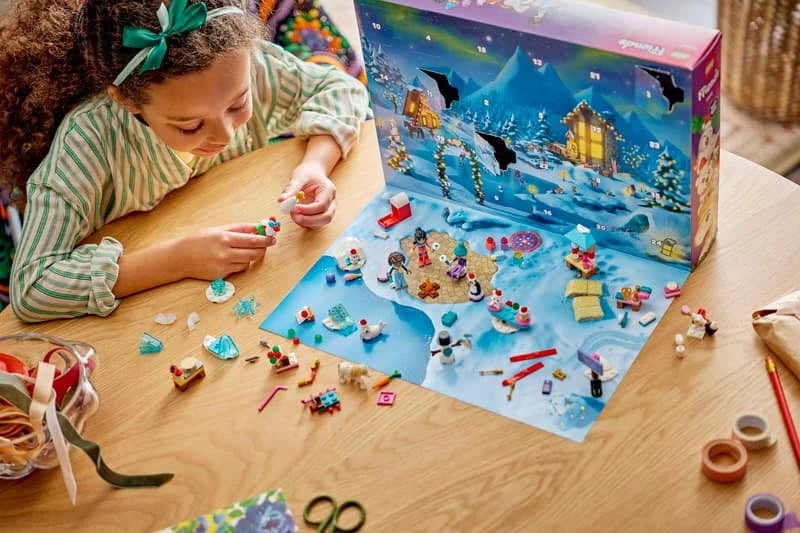 Child assembling LEGO Friends Advent Calendar pieces at a table with the opened winter calendar behind