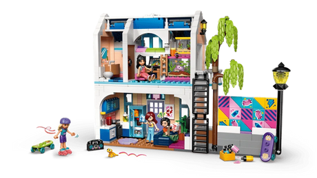Rear view of LEGO Friends Liann's Family House 42687 showing the open two storey interior, furnished rooms, minidolls, outdoor skate area, climbing ladder and colourful wall mural.