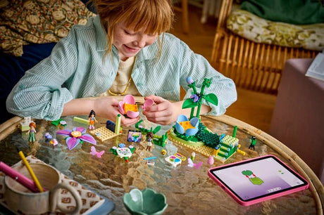 Child building the LEGO Friends Spinning Flower & Fairy Teacup Ride set on a table with a tablet nearby