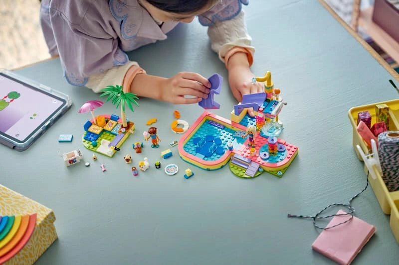 Child building LEGO Friends Fun Water Park Day with pieces and instructions on the floor