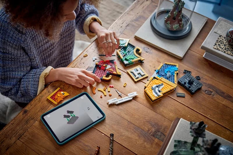Child building a LEGO Hogwarts house crest set at a table with pieces, display model and tablet instructions