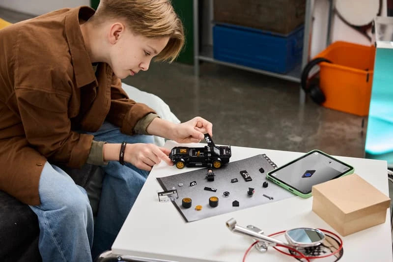 Child building a LEGO black car model at a table with loose pieces and tablet instructions