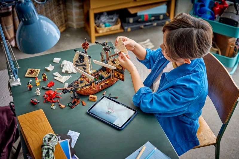 Child building LEGO Iconic Pirate Ship at a table with instructions, tablet and loose pieces visible
