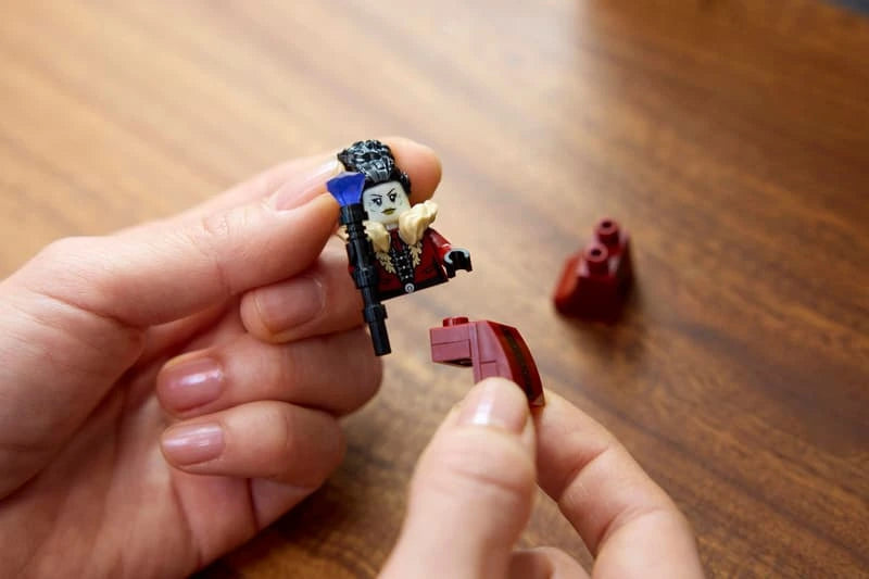 Hands holding a red and black LEGO minifigure and a dark red curved brick