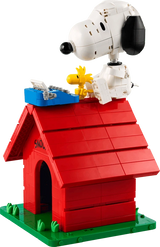 Brick built LEGO Snoopy seated on the red doghouse roof beside Woodstock and a blue typewriter, with the model on a green base.